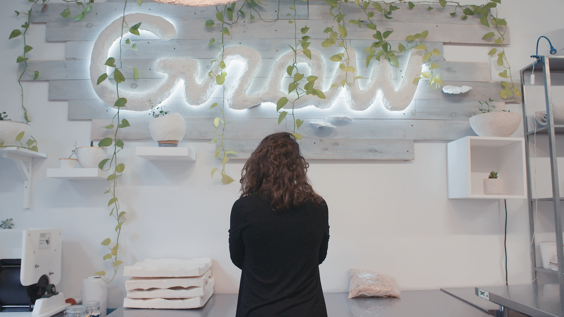 A woman looking at a white office wall with a lit sign that says Grow