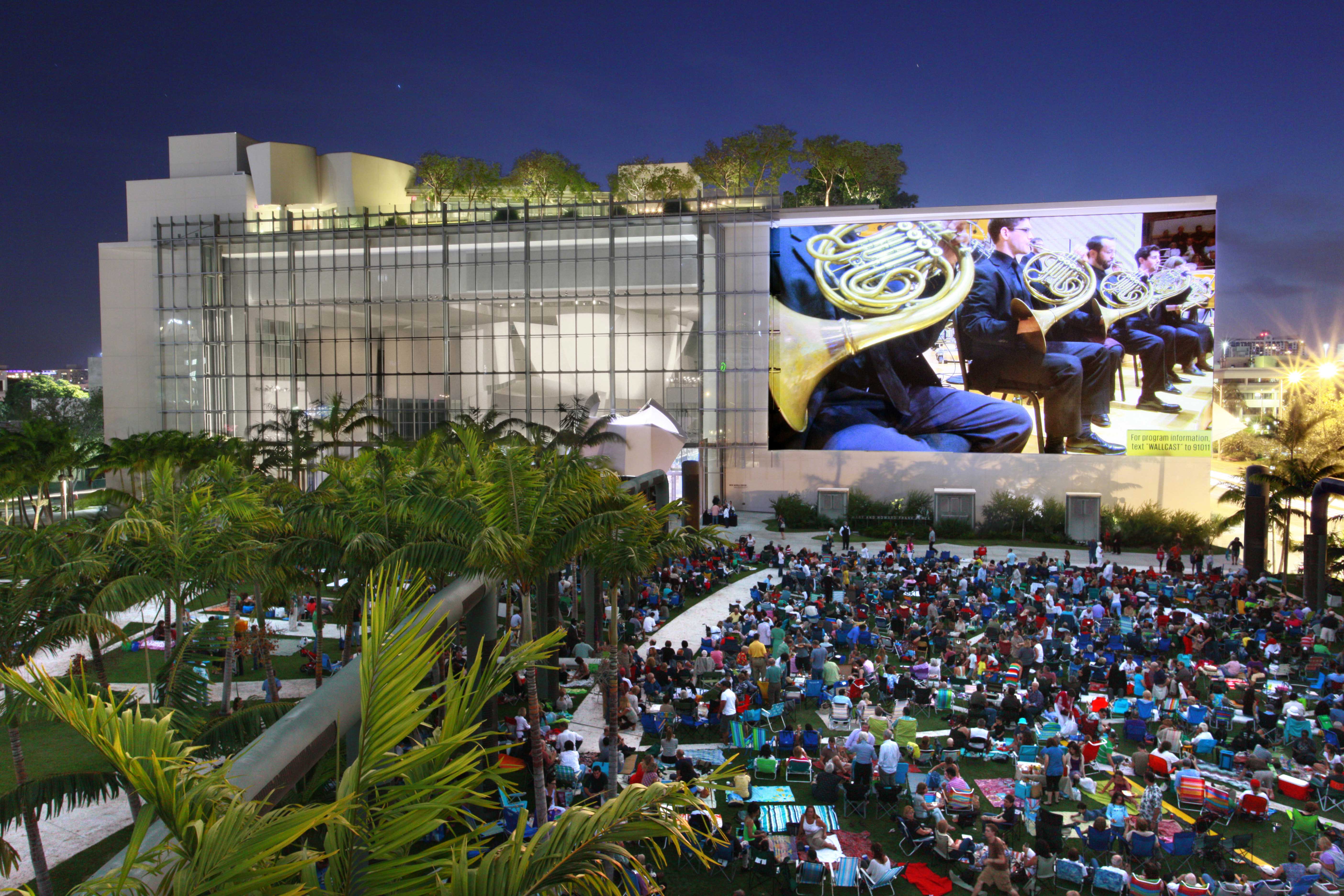A crowd watching an outdoor projection of a symphony performance