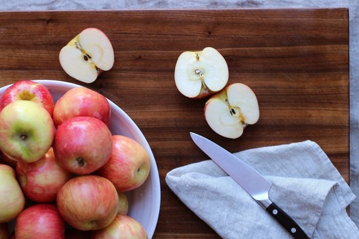A bowl of apples next to a knife and a few halved apples