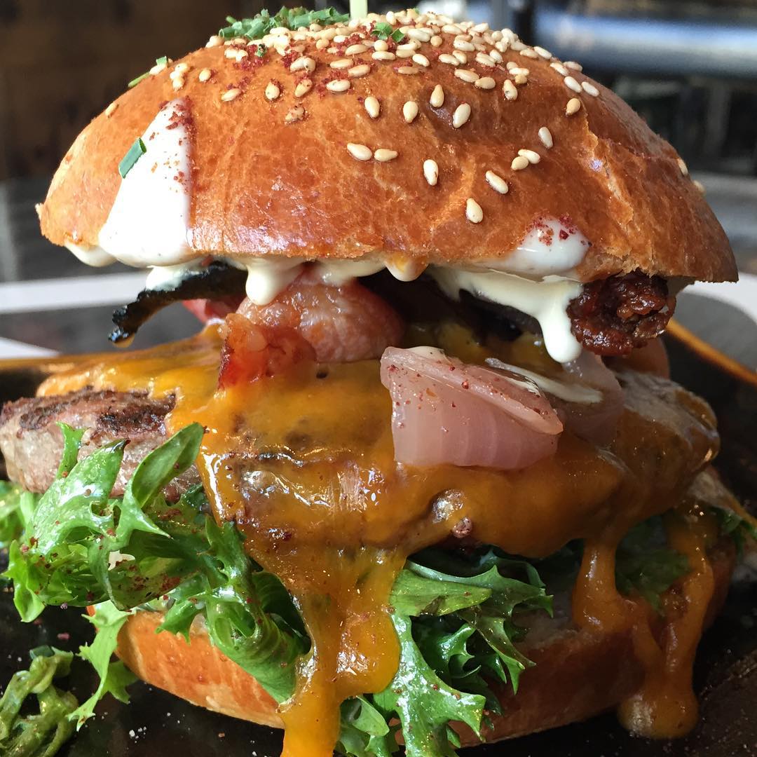 A close-up of a bacon cheeseburger with sauce and lettuce on a sesame seed bun 