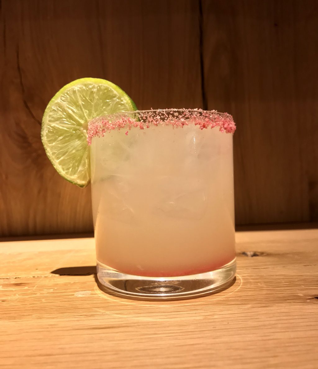 A pink cocktail with a pink sugar rim