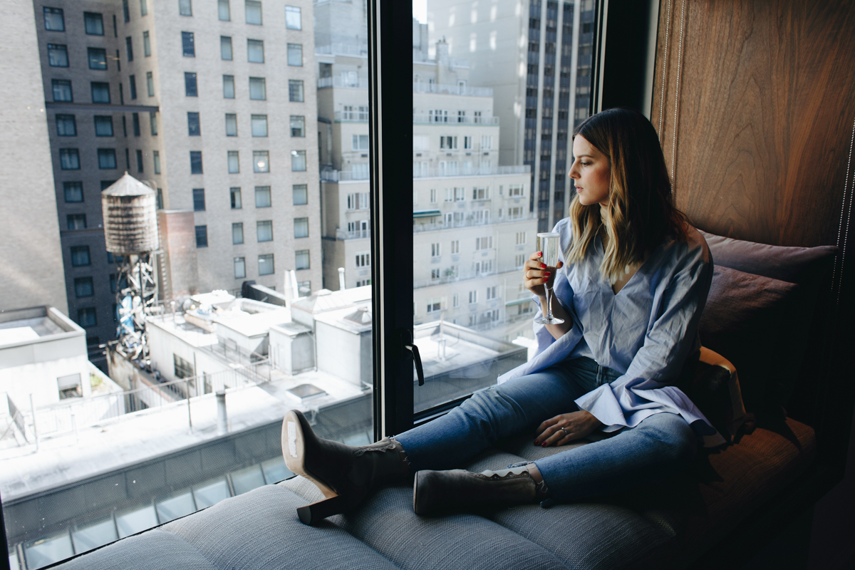 A woman drinking wine in a window nook overlooking Manhattan