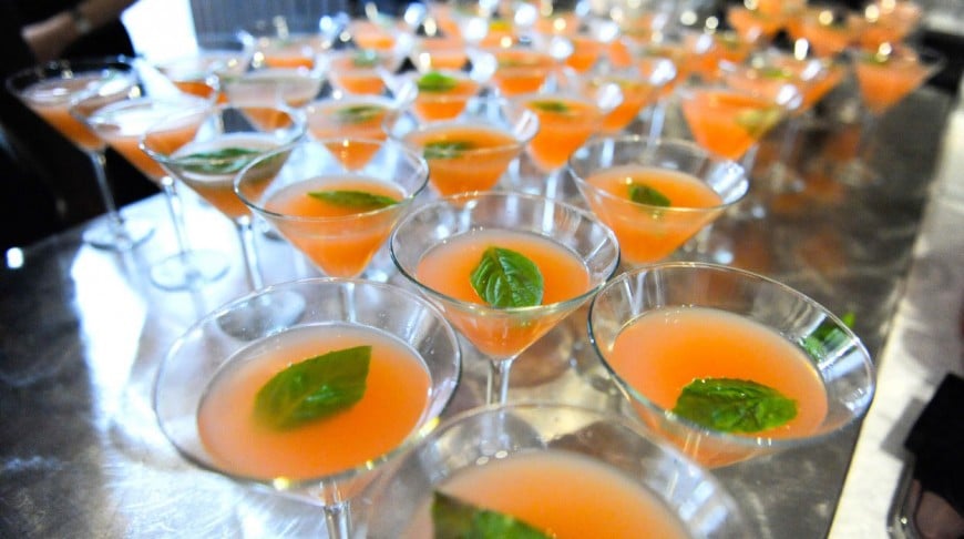 Many martini glasses with peach colored drink and floating mint leaves.