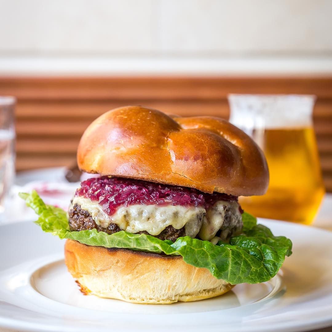 A large meat patty on a puffy potato bun with lettuce, cheese, and jelly