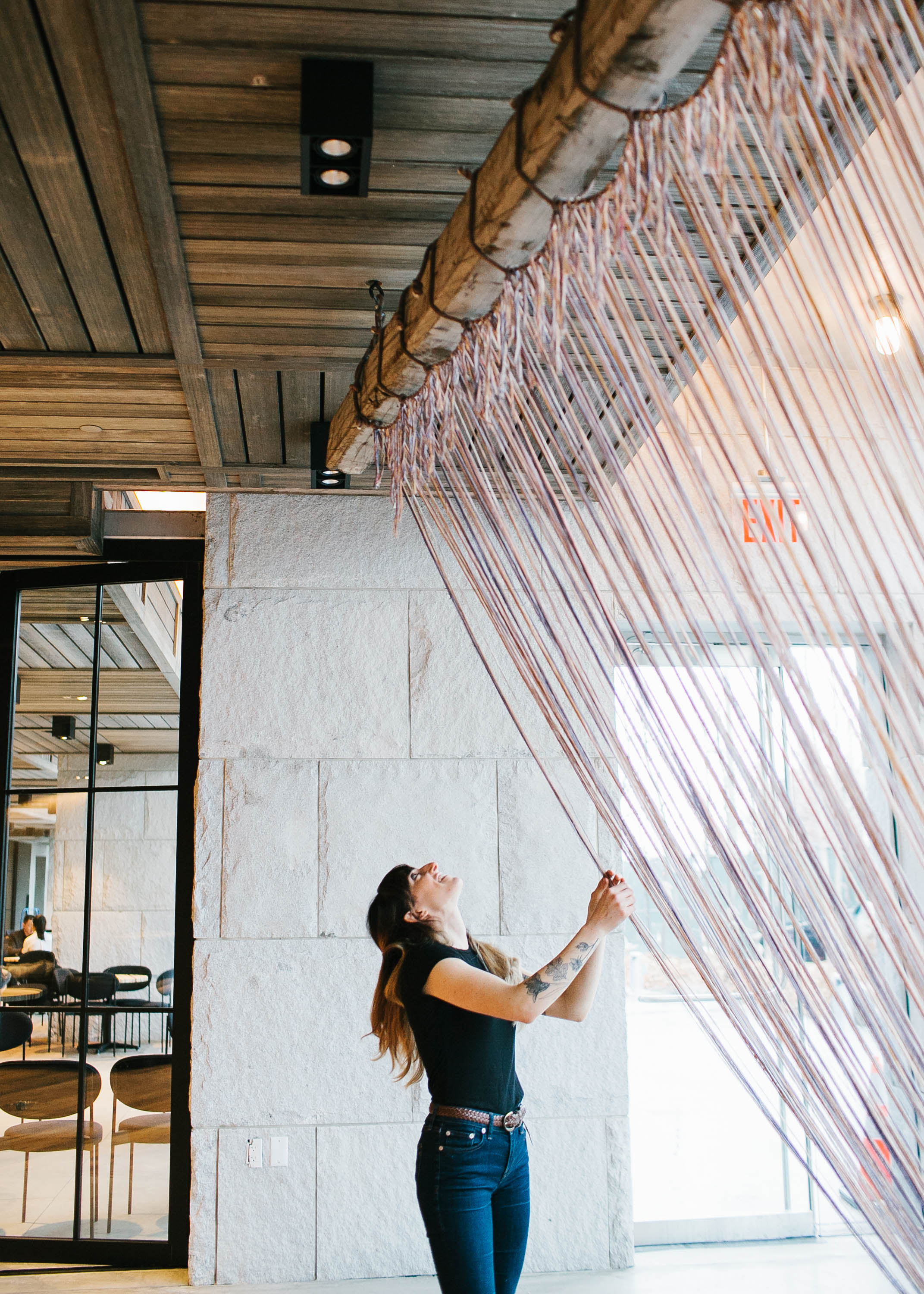 A woman hanging long strings of fabric from a wooden beam