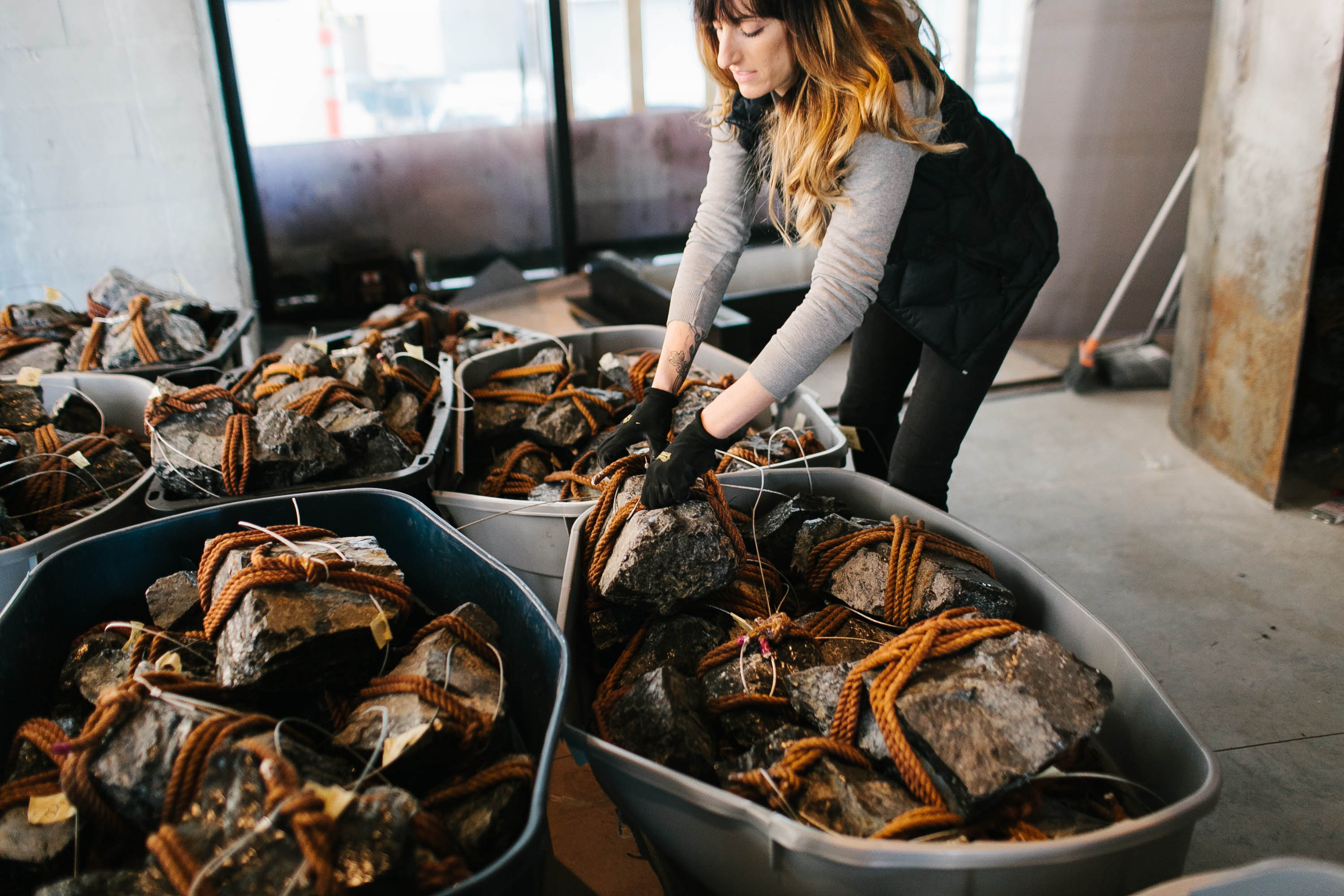 A woman going through bins filled with rocks tied with orange rope.