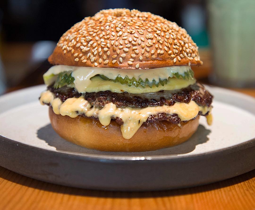 A burger on a sesame seed bun dripping with mayo and sauce