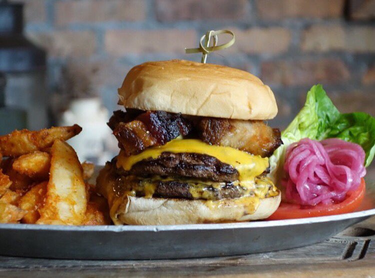 A double burger with cheese and smoked pork on a plate with fried potato wedges