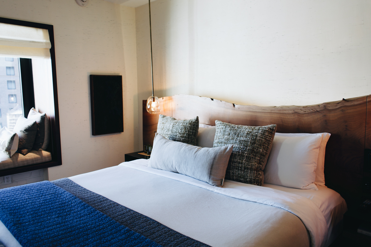 A hotel suite with a bed with a wooden headboard and cozy linens