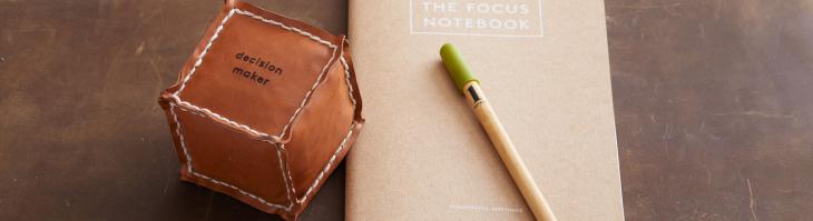 A leather dice labeled "Decision maker" sits left of a notebook labeled "The Focus Notebook"