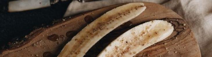 A banana sliced lengthwise rests atop a rustic wooden platter