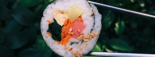 sushi roll held by chopsticks with leafy background