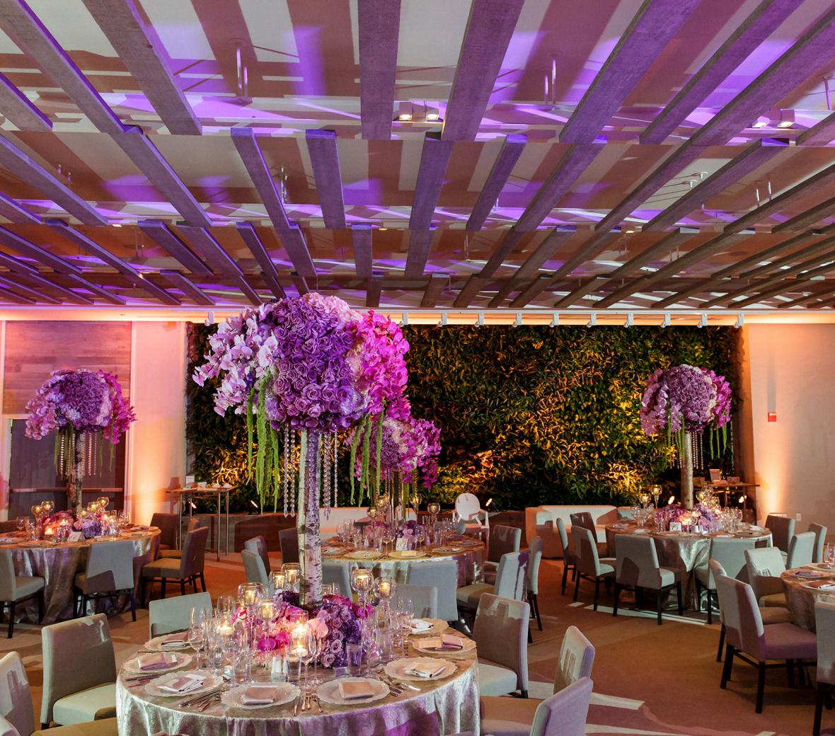 Wedding ballroom with floral arrangements on tables and pink and purple mood lighting