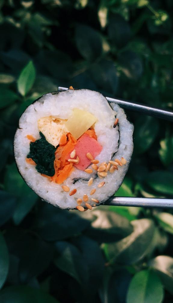 sushi roll held by chopsticks with leafy background