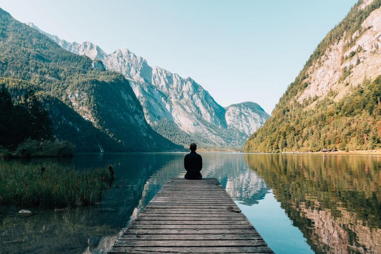 Man Sitting on Dock of Lake with Mountains